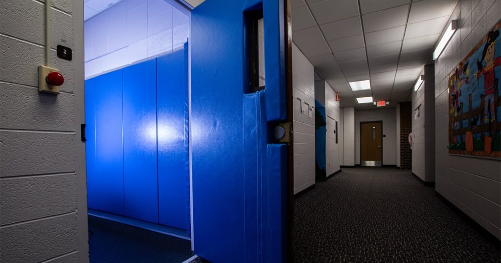 Blue padded seclusion room used in schools, showing an enclosed space designed for adult-controlled isolation with no visible exit choice.